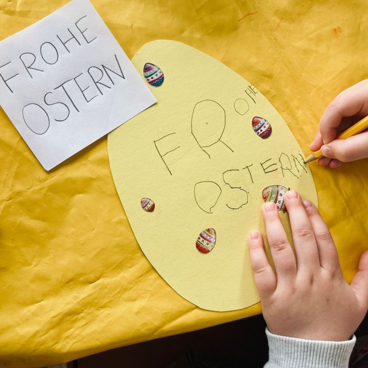 Kind schreibt Frohe Ostern auf gebasteltes Osterei