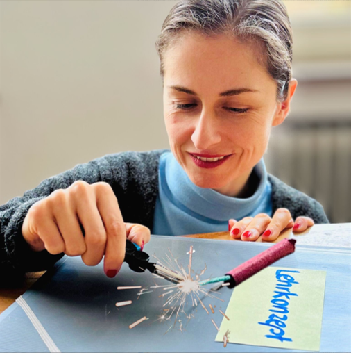 Jacqueline Sammet zündet einen Silvesterknaller an. Darunter liegt eine Mappe mit der Aufschrift "Lernkonzept".