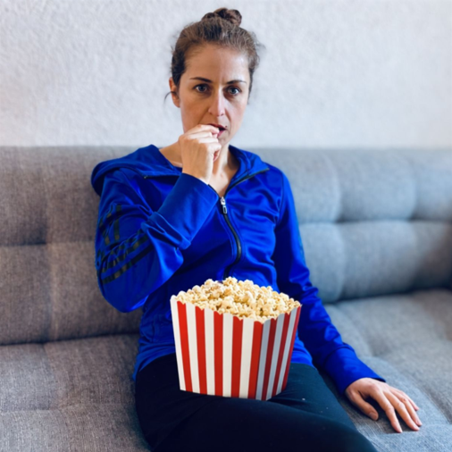 Jacqueline Sammet sitzt mit einer Popcorn-Tüte auf der Couch und isst Popcorn.